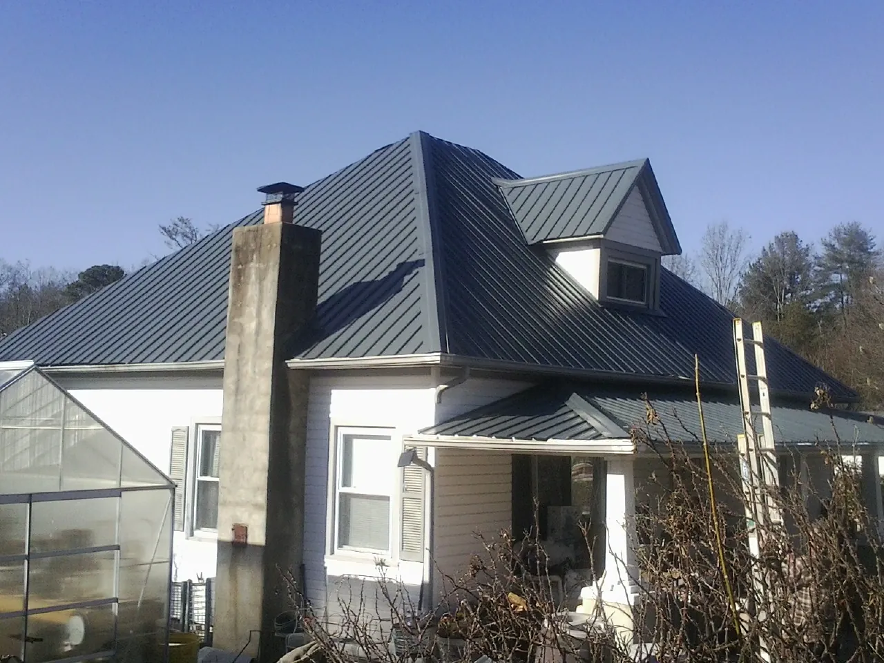 Dark blue standing seam metal roof on a white farmhouse with dormer — Slate & Tile Roof Repair by Roofing Brothers in Lufkin