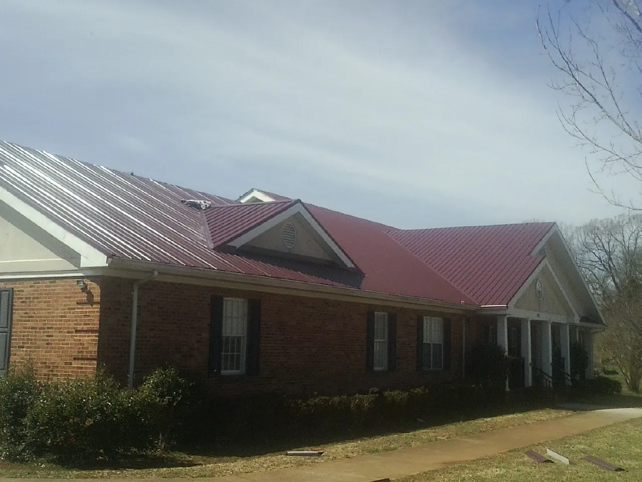 Red metal roof with gabled entries on a long brick building, from a Hail Damage Roof Repair job in Lufkin