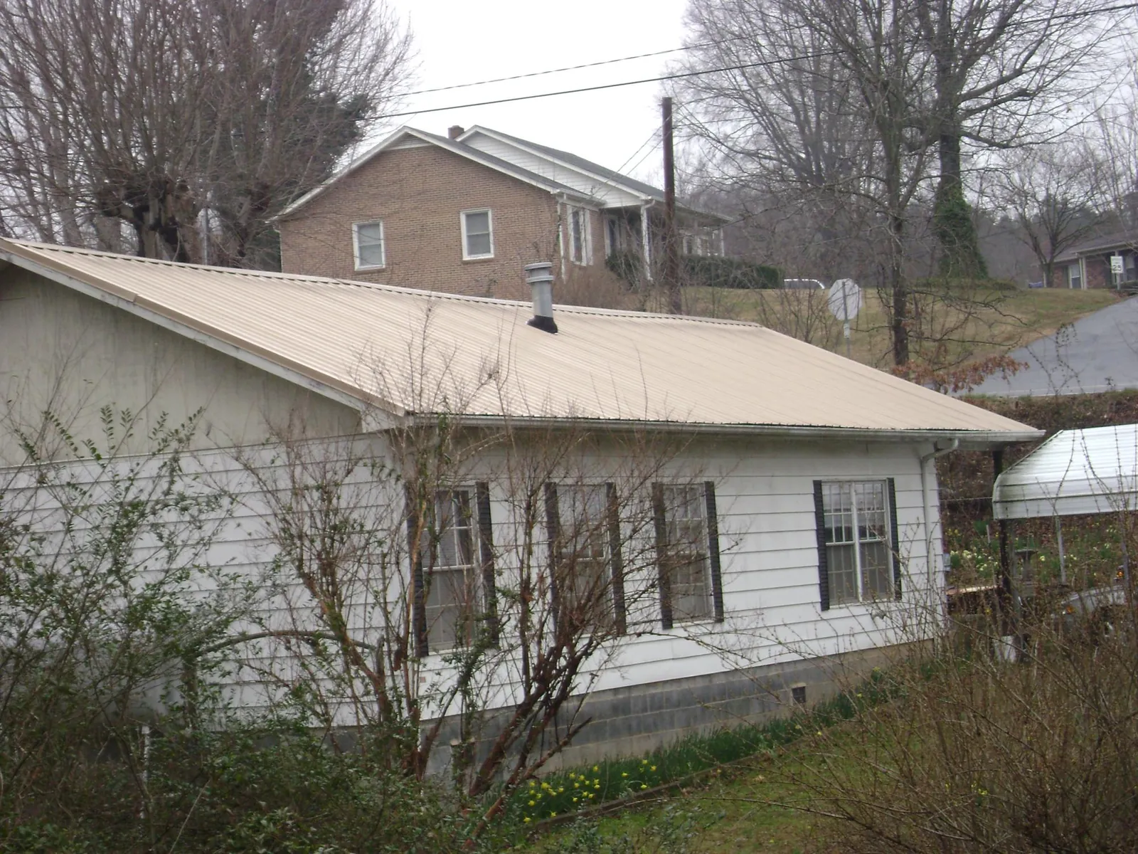 Tan metal roof on a white sided house set into a hillside — Commercial Roofing by Roofing Brothers in Lufkin