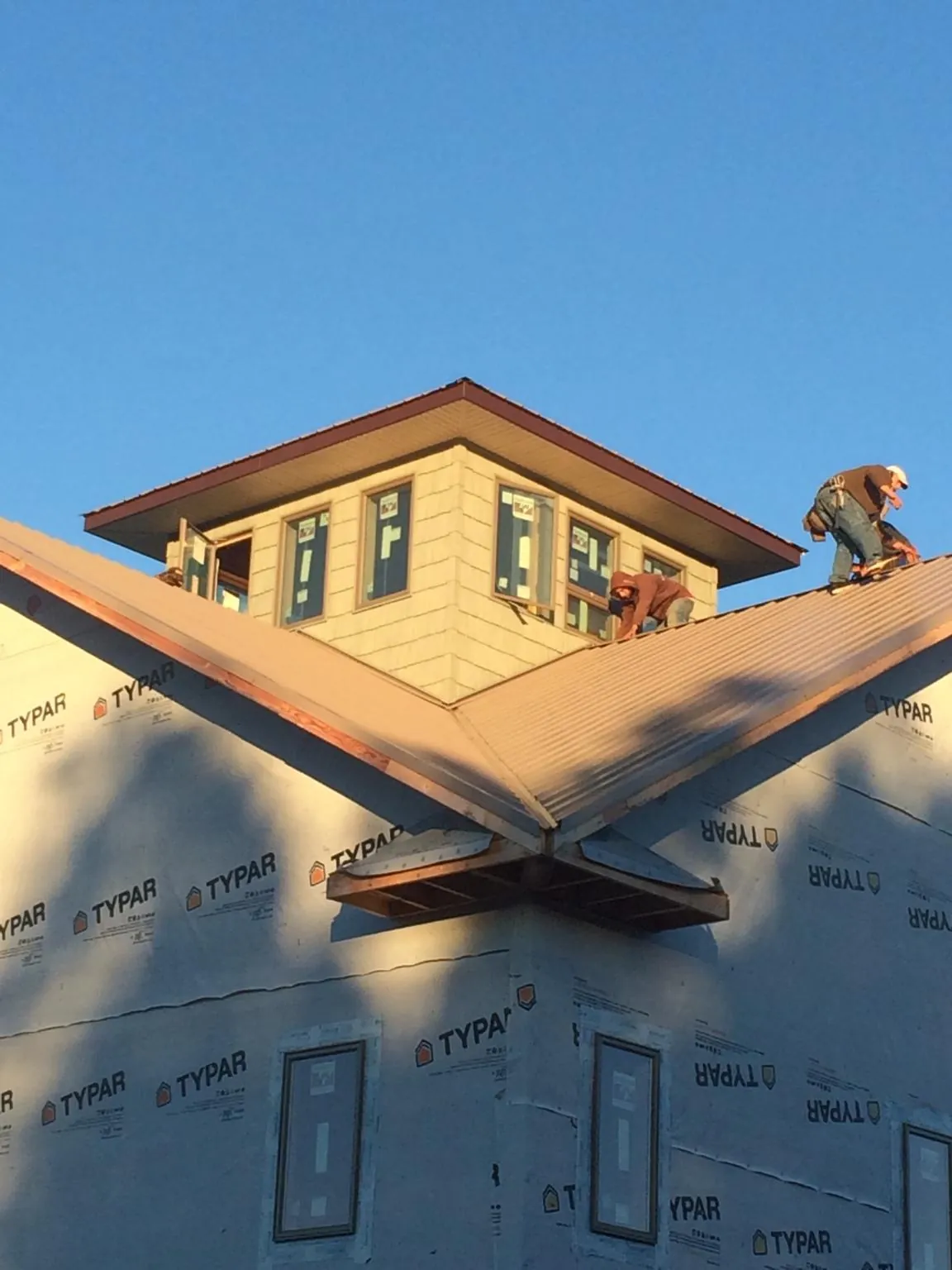 Roofers working around a rooftop cupola on a new metal roof at sunset — Roof Waterproofing in Lufkin by Roofing Brothers
